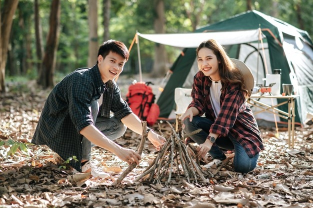 pretty-camper-girl-preparing-firewood-with-boyfriend-start-campfire-young-tourist-couple-helping-picking-branches-put-them-together-front-camping-tent_1150-48376